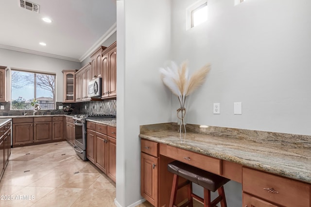 kitchen with light stone countertops, backsplash, ornamental molding, and stainless steel appliances