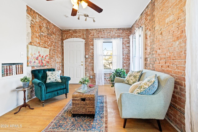 living area featuring hardwood / wood-style flooring, ceiling fan, and brick wall