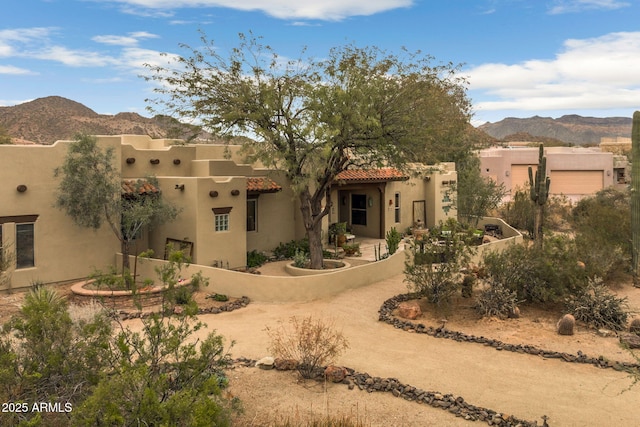 adobe home featuring fence, a tile roof, a mountain view, and stucco siding