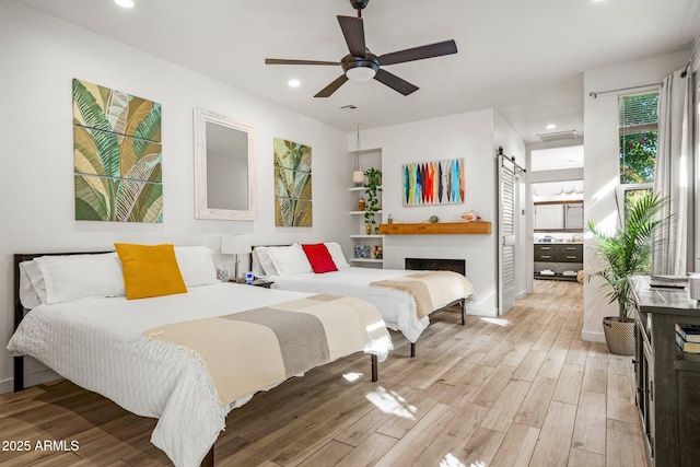 bedroom with light wood-style floors, recessed lighting, a ceiling fan, and a barn door