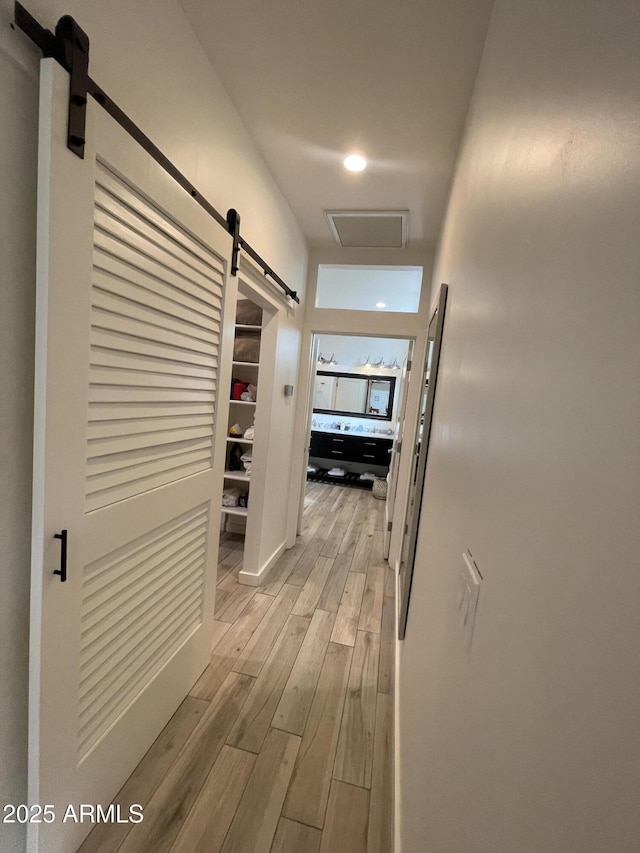 hallway with a barn door, visible vents, and light wood-style floors