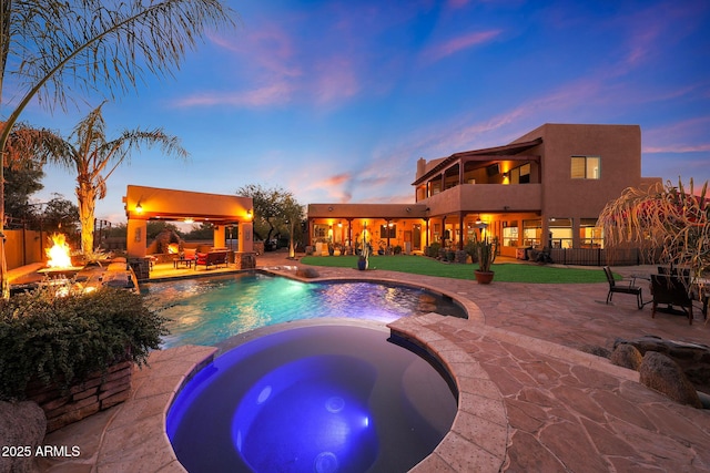 pool at dusk with a lawn, an in ground hot tub, an outdoor fire pit, a gazebo, and a patio area