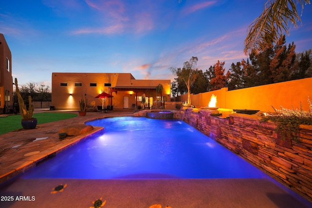 pool at dusk with pool water feature, an in ground hot tub, and a patio