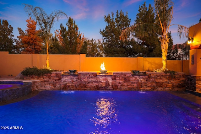 pool at dusk featuring an in ground hot tub and pool water feature