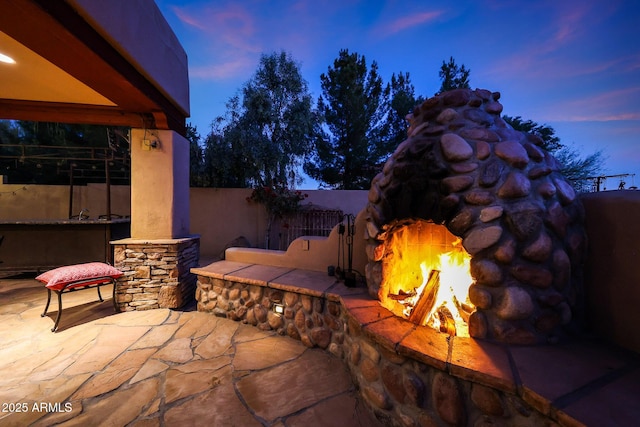 patio terrace at dusk featuring an outdoor stone fireplace