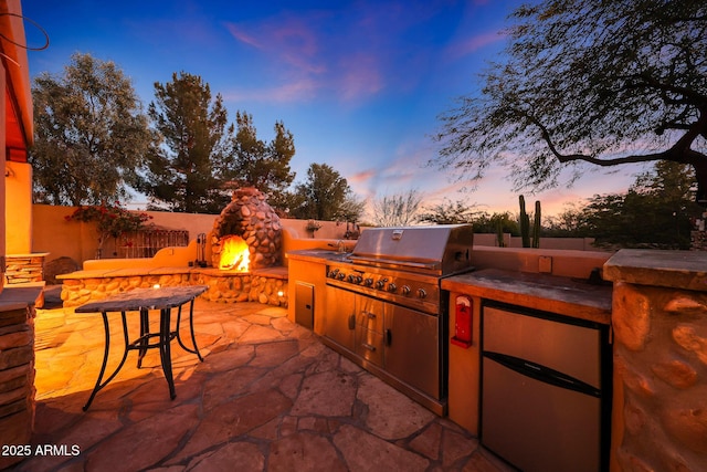 patio terrace at dusk featuring area for grilling, a grill, and an outdoor fireplace