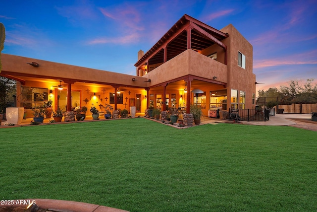 back house at dusk featuring a balcony and a lawn