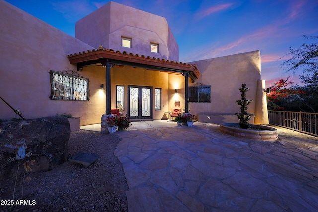 back house at dusk featuring french doors and a patio