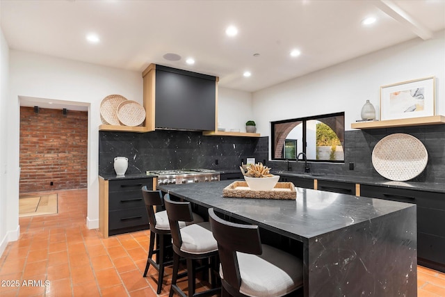 kitchen featuring sink, a breakfast bar, range hood, a center island, and tasteful backsplash