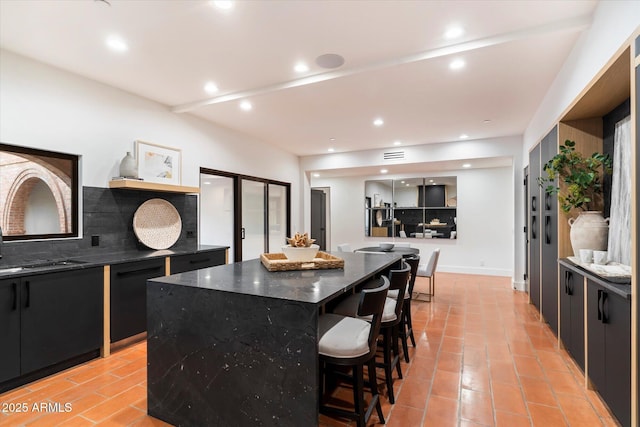 kitchen with light tile patterned flooring, a breakfast bar, black dishwasher, dark stone countertops, and a large island