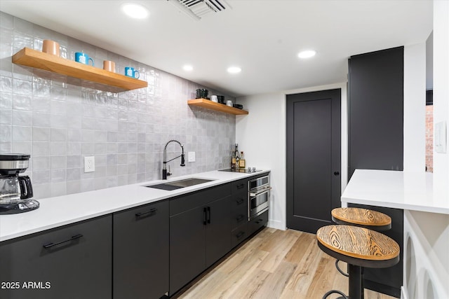 kitchen featuring sink, light wood-type flooring, decorative backsplash, stainless steel oven, and black electric cooktop