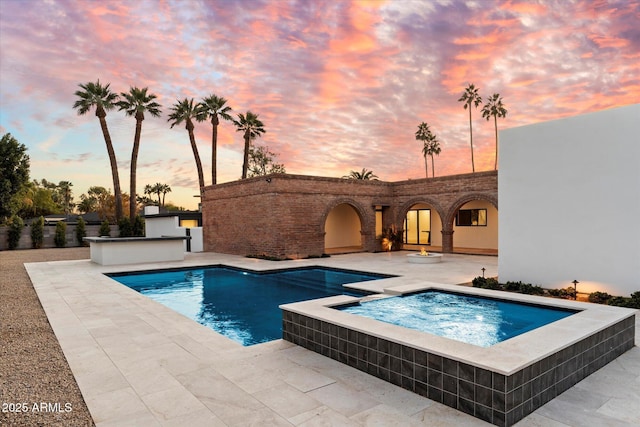 pool at dusk with an in ground hot tub and a patio area