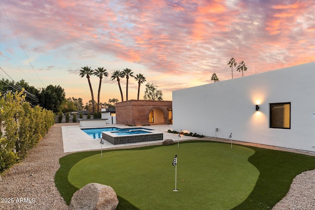 pool at dusk with a patio area and an in ground hot tub