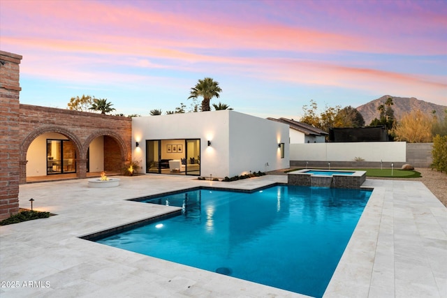 pool at dusk with a mountain view, a patio, and an in ground hot tub