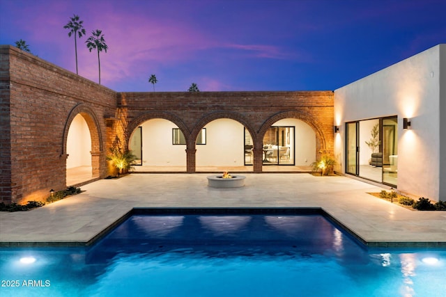 pool at dusk with an outdoor fire pit and a patio