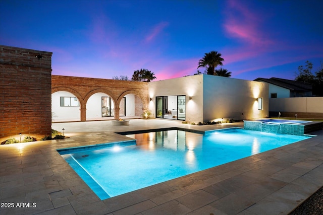 pool at dusk featuring a patio area and an in ground hot tub