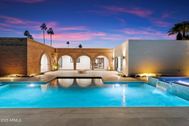 pool at dusk featuring pool water feature and a patio area