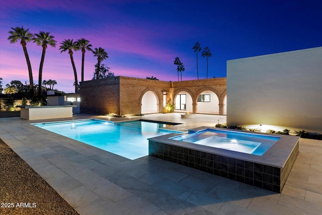 pool at dusk featuring an in ground hot tub and a patio