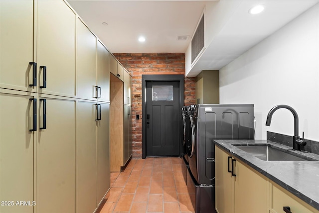 laundry area featuring washer and dryer, sink, cabinets, and brick wall