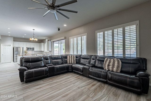 living room featuring ceiling fan with notable chandelier and light wood-type flooring