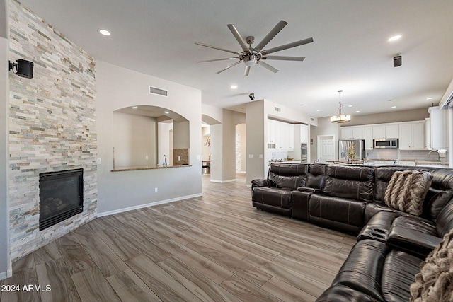 living room featuring a stone fireplace, light wood-type flooring, ceiling fan, and sink