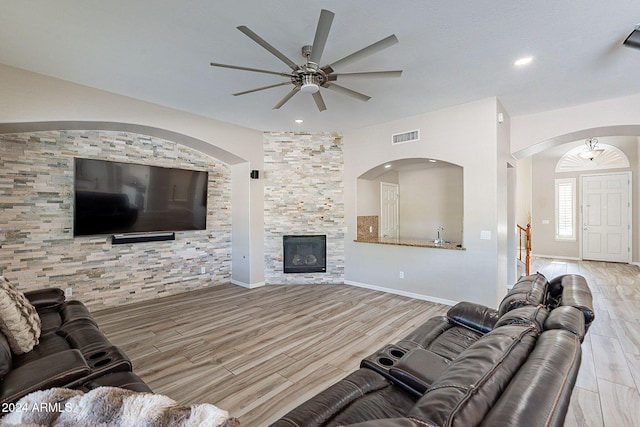 living room with a stone fireplace, light hardwood / wood-style floors, and ceiling fan