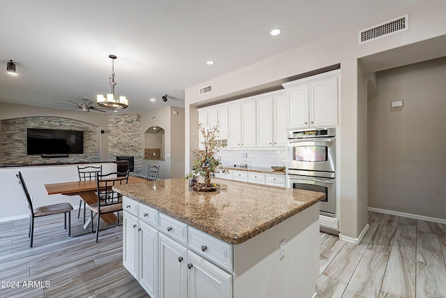 kitchen featuring pendant lighting, a center island, stainless steel double oven, light stone countertops, and white cabinetry