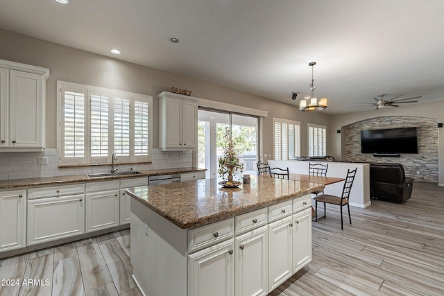 kitchen with tasteful backsplash, a kitchen island, sink, white cabinets, and ceiling fan with notable chandelier