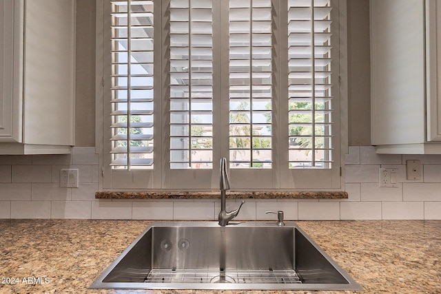 kitchen with decorative backsplash, white cabinetry, sink, and light stone counters