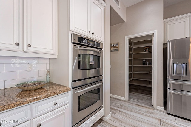 kitchen with white cabinetry, appliances with stainless steel finishes, backsplash, and dark stone countertops