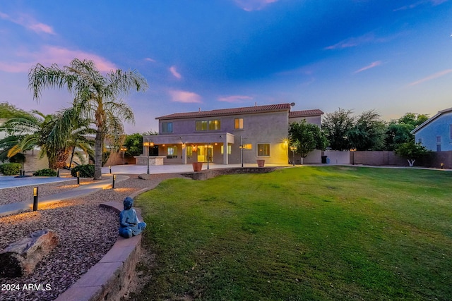 back house at dusk with a patio and a yard