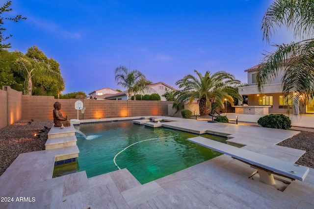 pool at dusk with a diving board, a patio, and pool water feature