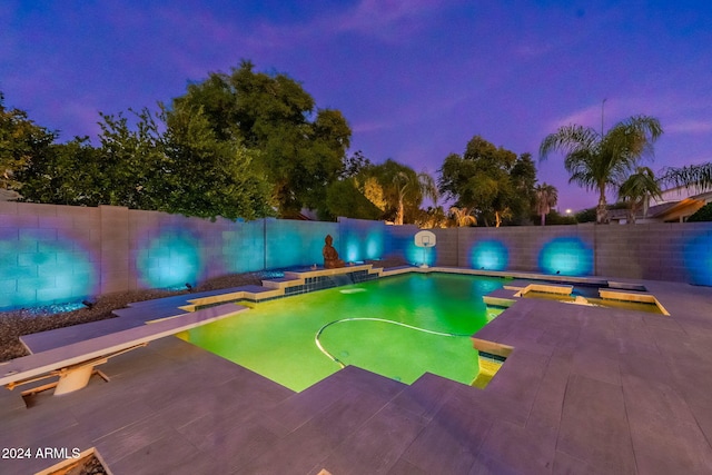 pool at dusk with a patio and a diving board