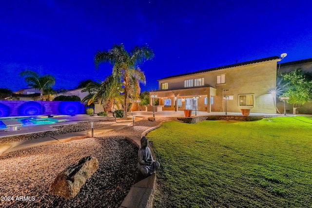 back house at night featuring a lawn and a patio area