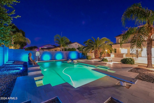 pool at night with a patio and a diving board