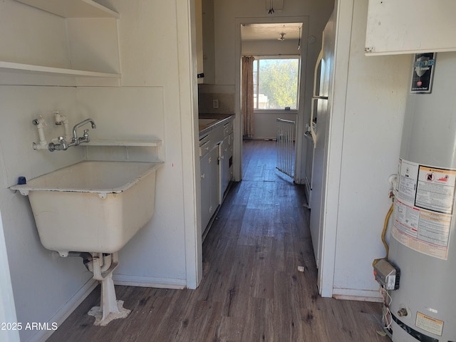 kitchen featuring dark wood-type flooring, baseboards, light countertops, water heater, and a sink