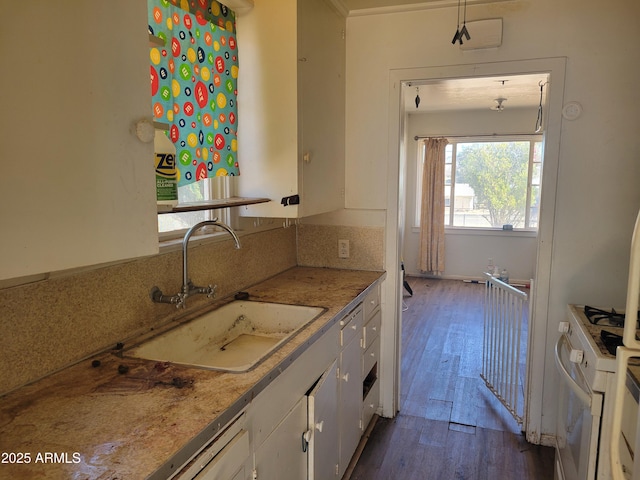 kitchen with dark wood-type flooring, light countertops, white range with gas stovetop, white cabinetry, and a sink