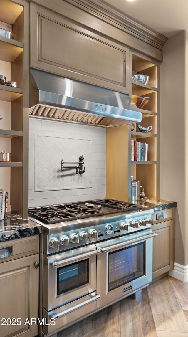 kitchen with dark stone counters, range with two ovens, tasteful backsplash, light hardwood / wood-style floors, and extractor fan