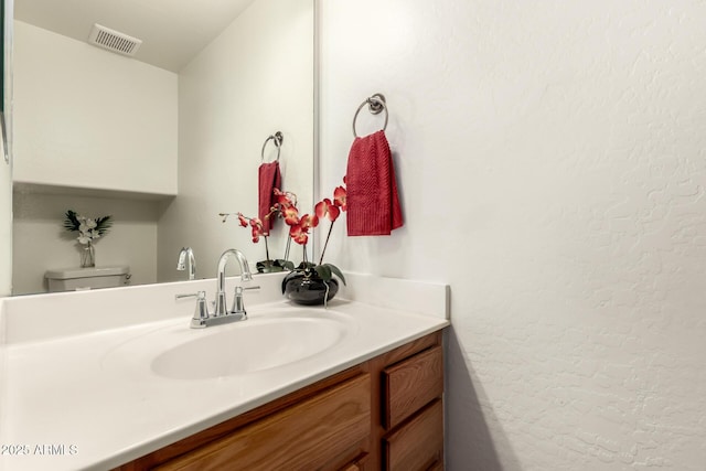 bathroom featuring visible vents, toilet, vanity, and a textured wall