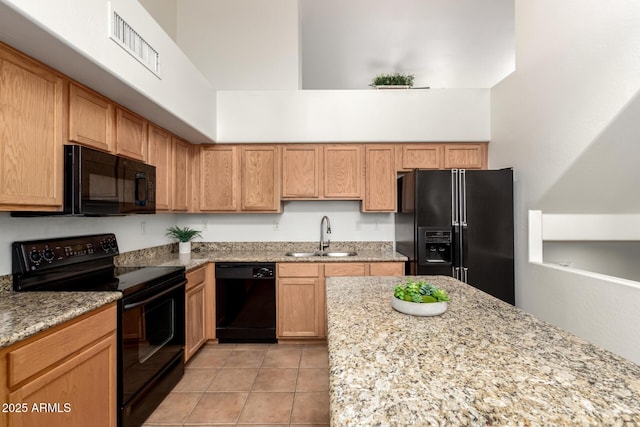 kitchen featuring light tile patterned floors, light stone counters, a sink, black appliances, and a towering ceiling