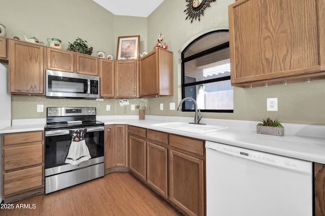 kitchen featuring brown cabinetry, a sink, light countertops, light wood finished floors, and stainless steel appliances