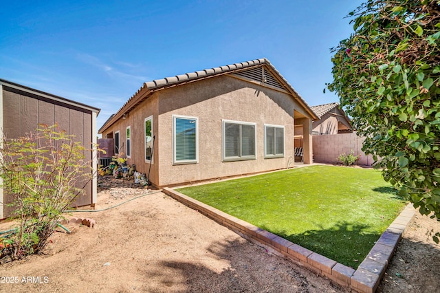 back of house with a lawn, a tiled roof, a fenced backyard, and stucco siding