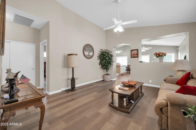 living room featuring arched walkways, a ceiling fan, baseboards, wood finished floors, and visible vents