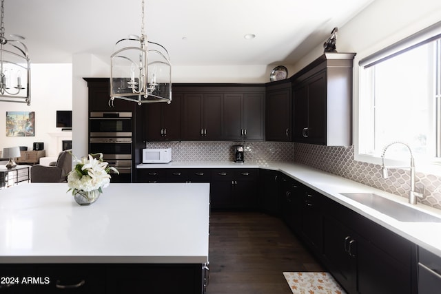 kitchen with pendant lighting, backsplash, stainless steel double oven, and sink