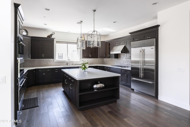 kitchen with appliances with stainless steel finishes, dark hardwood / wood-style flooring, decorative light fixtures, and a kitchen island