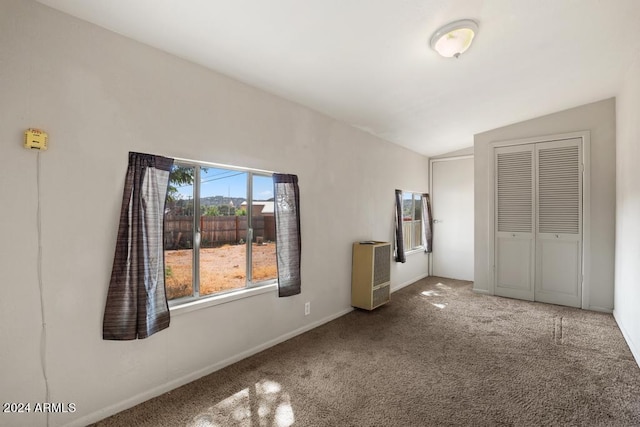 unfurnished bedroom with heating unit, lofted ceiling, carpet floors, and a closet