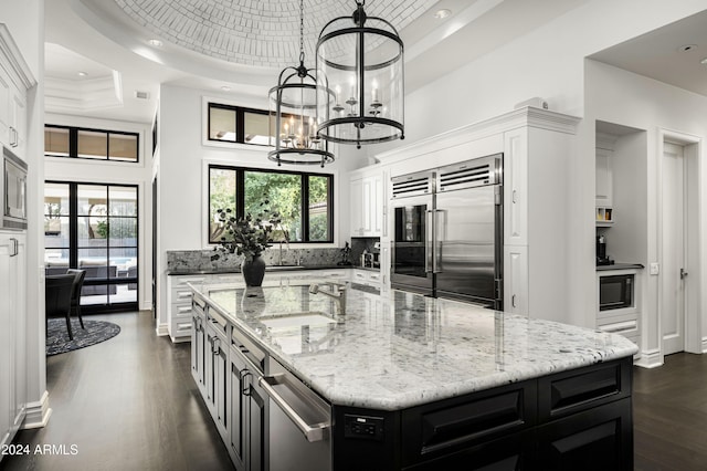 kitchen with sink, a center island, built in appliances, a chandelier, and white cabinets