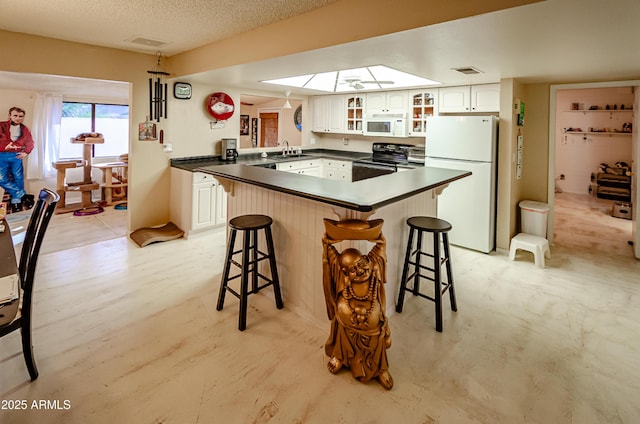 kitchen featuring kitchen peninsula, white appliances, a breakfast bar area, and white cabinets