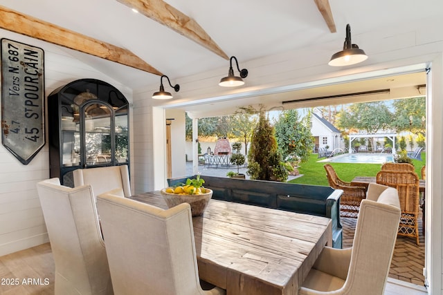 dining space with lofted ceiling with beams, light wood-type flooring, and wooden walls