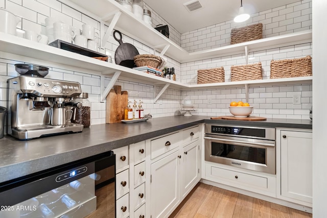 kitchen featuring stainless steel appliances, white cabinets, light wood-type flooring, and decorative backsplash